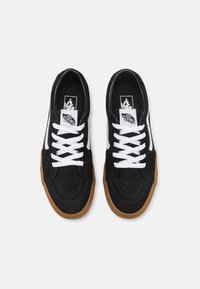 Ett par svarta Vans-sneakers med vita snören, vit sidestreck, gummisula och "Off The Wall"-logotyp på tungan, sett från ovan.