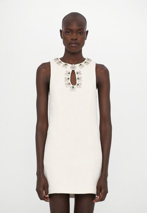 White sleeveless dress with a textured fabric, featuring a keyhole neckline adorned with floral embellishments in pink and green.