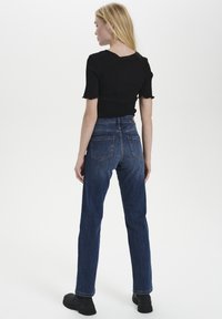 Top corto a maniche corte a coste nere abbinato a jeans in denim scuro a vita alta. I jeans presentano due tasche posteriori e una vestibilità dritta.
