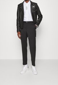 Zwarte leren motorjack, wit overhemdd met afdrukdetails, grijze op maat gemaakte broeken en witte sneakers. Minimalistisch design.