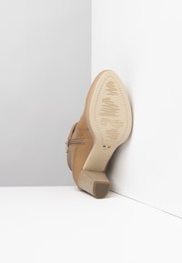 Stivale alla caviglia in pelle color cuoio con tacco a blocco beige texturizzato. Presenta una cerniera laterale e una suola dettagliata con motivi in rilievo.