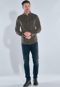 Braun gemusterte Langarmhemd mit Knopfleiste, kombiniert mit dunkelblauen Jeans und schwarzen Schnürstiefeln. Einfaches Design mit einer Taschenapplikation.