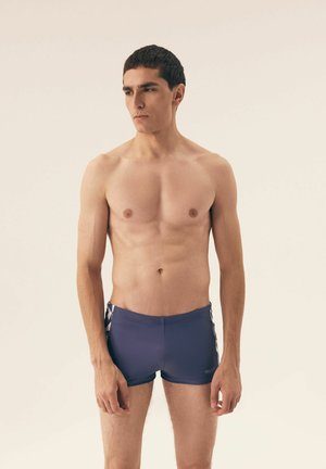 Men's swim trunks, short length, navy blue with white side accents. Smooth, stretchy fabric, minimal design, no visible logos or patterns.