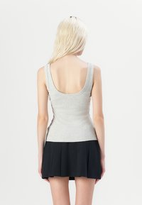 Top sin mangas gris de tejido suave con escote en la parte posterior, combinado con una mini falda negra con plisados. El conjunto presenta un diseño ajustado y una textura suave.