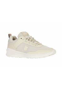 Zapatilla deportiva de color beige claro con parte superior de malla, suela de goma y un logotipo discreto. Punta redondeada, talón elevado y diseño de cordones.
