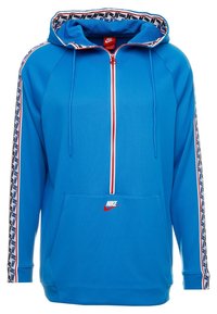 Sudadera azul con cremallera y capucha, cremallera roja y bolsillo frontal. Presenta un ribete estampado a lo largo de las mangas y un pequeño logo rojo en la parte frontal.