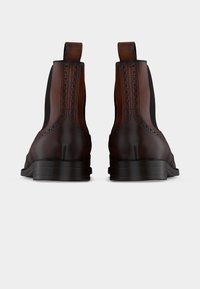 Paire de bottines Chelsea en cuir marron foncé avec détails brogue et panneaux latéraux élastiques noirs, vues de dos sur fond blanc.