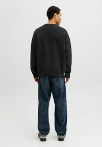 Czarna, oversize bluza z długimi rękawami, w połączeniu z luźnymi, granatowymi dżinsami. Tkanina wydaje się być miękka i ma teksturowane wykończenie.