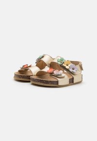 Guldiga sandaler tillverkade av syntetiskt material, med blommiga detaljer i rosa, gult och grönt. Korkliknande sula, öppen design.