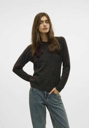 Pull long gris foncé en tricot doux, avec un col rond et des poignets côtelés, associé à un jean bleu clair à coupe décontractée.