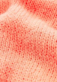 Dzianina w miękkim koralowym kolorze z teksturowaną powierzchnią, z wzorami ściągaczowymi i cienkimi nitkami wplecionymi dla przytulnego wyglądu.