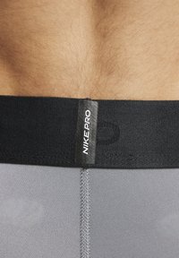 Grå idrettsshorts har et svart elastisk liv med 'NIKE PRO' merking. Stoffet har en glatt tekstur med synlige sømmer.