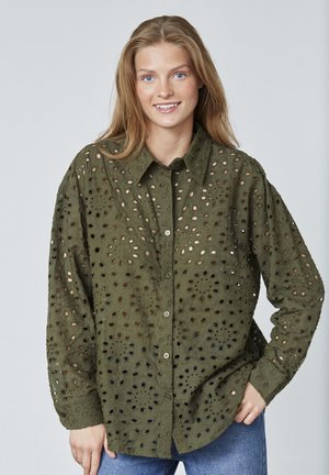 Olivengrøn, langærmet blouse med broderede udskæringsmønstre. Har en knaplukning foran og en afslappet pasform. Materialet er en bomuldsblanding.