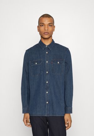 Camicia in denim blu scuro con colletto alla francese, due tasche frontali e bottoni bianchi. Presenta un taglio dritto con maniche lunghe.