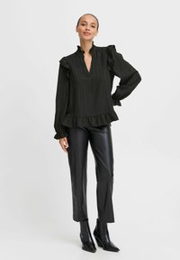 Blusa nera a strisce con colletto e maniche arricciate, abbinata a pantaloni in pelle nera aderenti e stivaletti a punta.