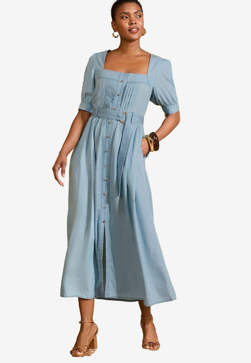 Light blue denim maxi dress with short puff sleeves, square neckline, front buttons, pleats, and a belted waist. Features a relaxed fit.