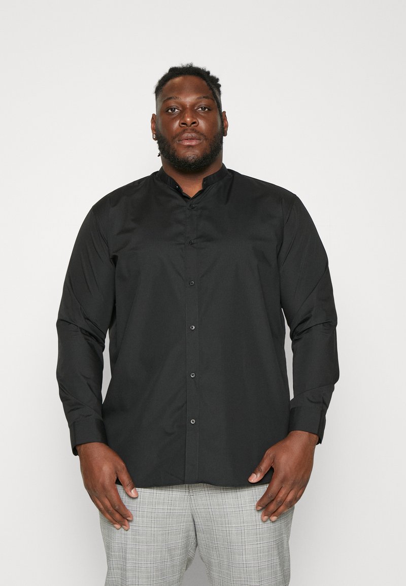 Schwarzes Langarmshirt mit Stehkragen, Frontknöpfen und glattem Stoff. Getragen mit grauen karierten Hosen, die eine taillierte Passform aufweisen.