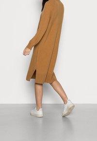 Lång, löst sittande brunstickad klänning i mjukt material, med sidslitsar och parat med vita sneakers.