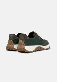 Green sneakers with a textured fabric upper, suede accents, and a brown rubber outsole featuring a rugged tread pattern. Rounded design.