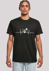 Schwarzes Baumwoll-T-Shirt mit einem weißen Herzschlag-Linien-Design, das ein Herz und Pfotenabdrücke in der Mitte zeigt. Entspannte Passform, Rundhalsausschnitt.