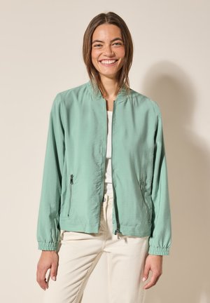 Svetle zelená bomber bunda s zipovým uzávěrem, dvěma bočními kapsami a elastickými manžetami. Hladká textura s lehkým designem.