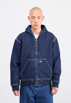 Felpa con cappuccio in denim blu scuro, con zip frontale, due ampie tasche, polsini a coste e cappuccio con cordino. Presenta cuciture a vista.