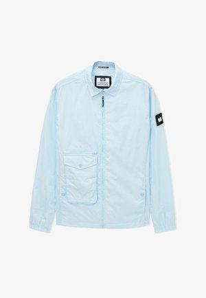 Vaaleansininen vetoketjullinen takki, jossa on kaulus, etutasku läpällä ja musta logoplaatta vasemmassa hihassa.