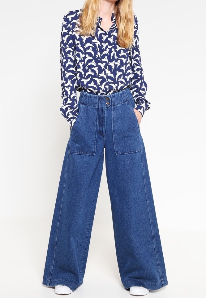 Camicetta navy con motivo di uccelli bianchi, colletto abbottonato, abbinata a pantaloni in denim blu a gamba larga con grandi tasche e vita alta.