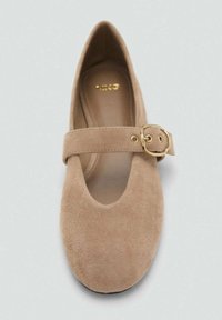 Beige mokasini Mary Jane dengan ujung bulat dan tali lebar yang menampilkan detail gesper emas. Bagian dalam yang halus tanpa pola yang terlihat.