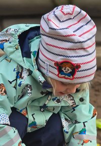 Valkoinen ja punaraitainen pipo, jossa on tyttöä esittävä patch. Mintunvihreä sadetakki, jossa on leikkisiä hahmojen kuvioita sinisessä ja mustassa.