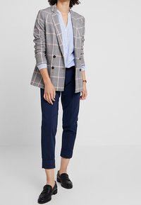 Dubbelt knäppt kavaj i grått med rutmönster och rosa accenter, kombinerad med en ljusblå skjorta och marinblå beskurna byxor. Svarta loafers.