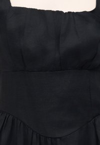 Robe noire sans manches avec tissu froncé au niveau de la poitrine et une large ceinture au-dessus d'une jupe évasée.
