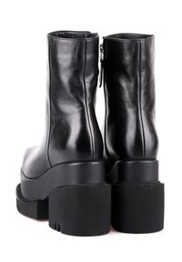 Paire de bottines en cuir noir avec semelles plateformes épaisses et talons carrés, vues de dos avec fermetures éclair latérales.
