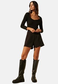 Top noir à manches longues côtelé avec un décolleté en scoop, associé à un short noir. Porté avec des bottes en cuir noires jusqu'aux genoux avec une semelle épaisse.