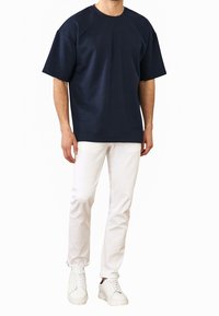 Camiseta de gran tamaño en color marino con mangas cortas, cuello redondo, hecha de una tela suave. Combinada con pantalones ajustados blancos y zapatillas blancas.