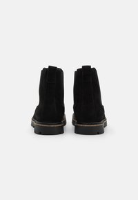 Bottines en suède noir avec une texture lisse, des languettes de tirage et une semelle en caoutchouc présentant une subtile couche de liège autour de la base.