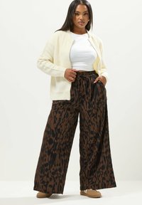 Vaalean kerman värinen neulecardigan valkoisen paidan päällä, yhdistettynä löysiin ruskeisiin leopardikuvioisiin hikepantalon. Ruskeat liukuhihna kengät täydentävät asun.