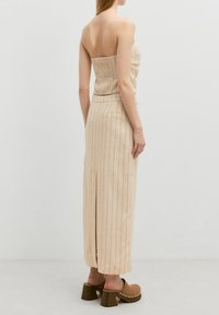 Beige trägerloses Oberteil mit gerafftem Rücken, kombiniert mit einem langen, beigen Nadelstreifenrock. Klobige braune Holzclogs mit Holzabsätzen runden das Outfit ab.