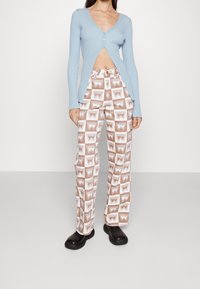 Vaaleansininen ribattukardigan, jossa on V-pääntie ja etupainikointi, yhdistettynä kuviollisiin ruskeisiin ja valkoisiin leveälahkeisiin housuihin, joissa on logosuunnittelu. Mustat kengät.