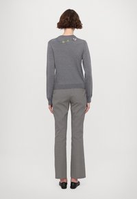 Szürke kötött pulóver virágos hímezéssel a nyakrésznél, fekete-fehér kutyafog mintás nadrággal és fekete cipővel párosítva.