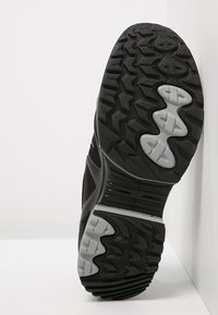 Schwarze Sportschuhsohle mit einer dicken Gummiaußensohle, die ein strukturiertes Profil und hellgraue Akzente für Grip und Stabilität aufweist.