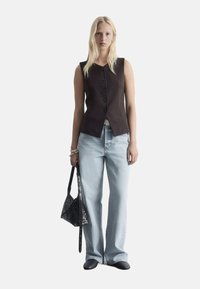 Brauner ärmelloser Weste mit Vorderknöpfen, kombiniert mit hellblauen weit geschnittenen Jeans. Eine schwarze strukturiert-handtasche und flache Schuhe runden den Look ab.