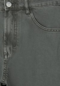 Gros plan sur la poche d'un jean denim gris foncé, bouton argenté et passants de ceinture montrant la texture du tissu et les détails des coutures.