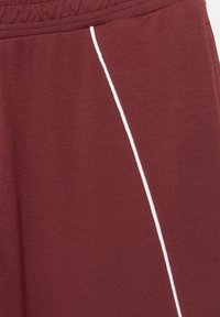 Bordeaux jogger med en struktureret finish, med en hvid sidestribe. Elastisk talje for en sikker pasform, velegnet til afslappet brug.