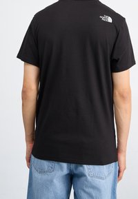 Černé bavlněné tričko, krátké rukávy a kulatý výstřih. Na horní části zad se nachází bílé logo. V kombinaci s modrými džíny.