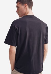 Černé bavlněné tričko s kulatým výstřihem a krátkými rukávy, hladkou texturou a volným střihem, zobrazené ze zadní strany.