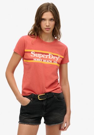 T-shirt en coton rouge à manches courtes, avec un logo blanc et des rayures jaunes. Associé à un short en denim noir et une ceinture noire.