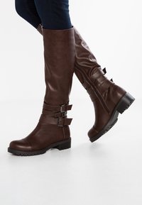 Botas marrones hasta la rodilla hechas de cuero sintético, con correas de hebilla, un cierre lateral y una suela con textura para mayor agarre.