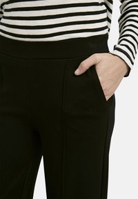 Schwarze, figurbetonte Hosen mit Seitentaschen. Aus glattem Stoff gefertigt, mit einem breiten Bund und dezenten Nahtdetails.