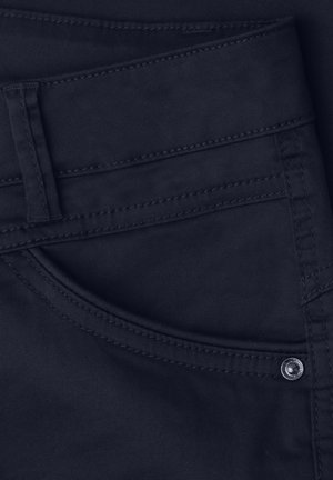 Jean en denim bleu marine foncé en gros plan montrant la poche avant, la boucle de ceinture et le détail du rivet métallique.